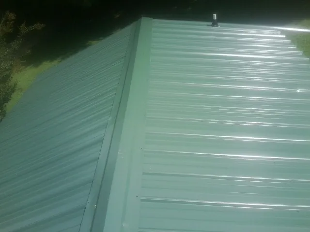 New green metal panels meeting at the ridge of a roof — Flat Roof Repair work by our crew in Corinth