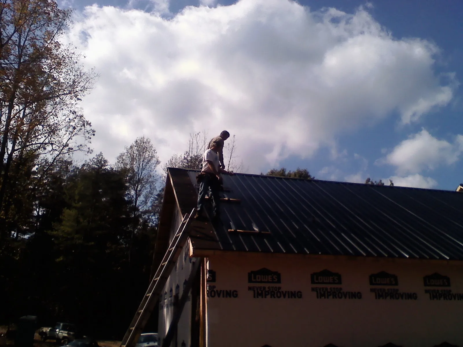 Roofer fastening dark metal panels high against a cloudy sky, from a Roof Inspection job in Corinth
